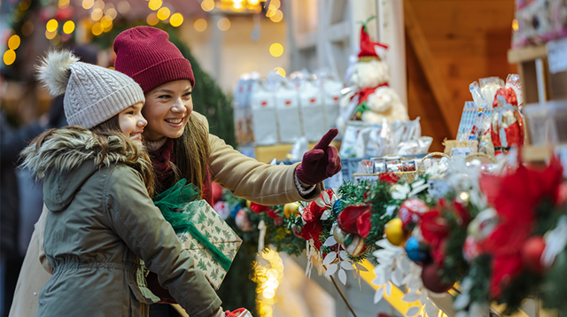 Mother and daughter browse a cheerful Christmas market, discovering gifts and decorations as twinkling lights and seasonal decor create a warm, joyful holiday atmosphere.